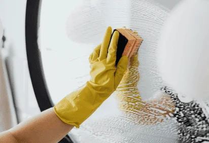 Person cleaning a shower glass door using a squeegee and wearing yellow gloves
