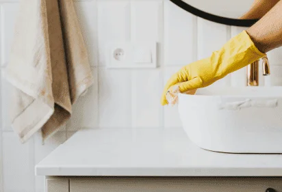 Person cleaning a shower glass door using a squeegee and wearing yellow gloves