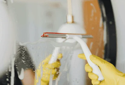 Close-up of a gloved hand scrubbing a mirror with a sponge and soap suds